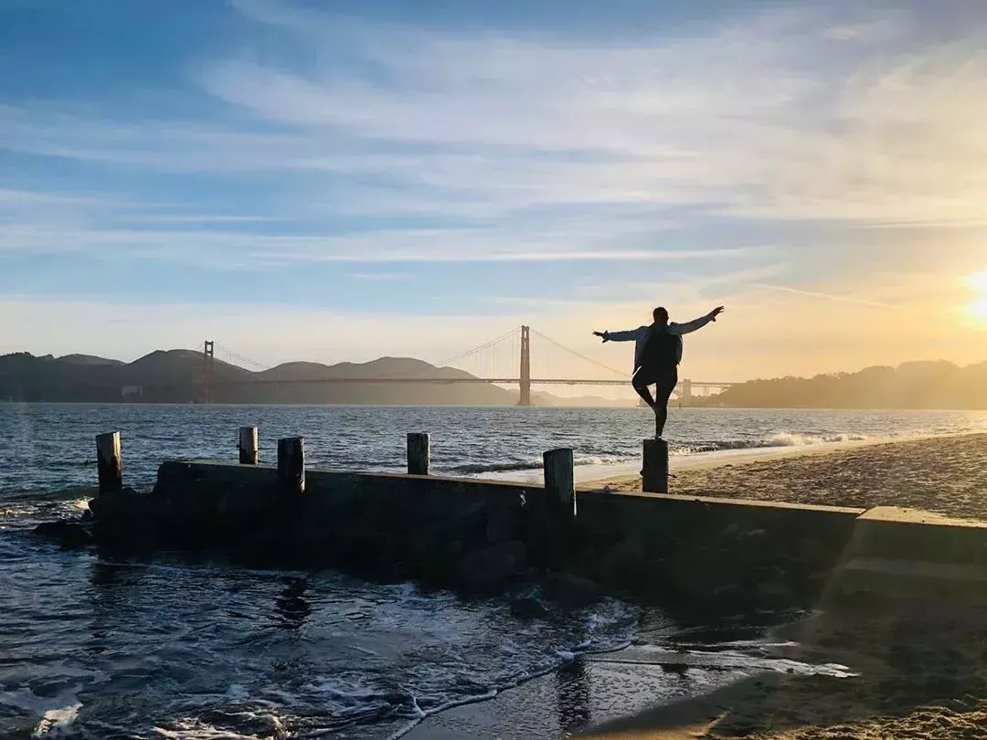 A woman stands on a pier in San Francisco's Marina neighborhood, looking out at the Golden Gate Bridge.